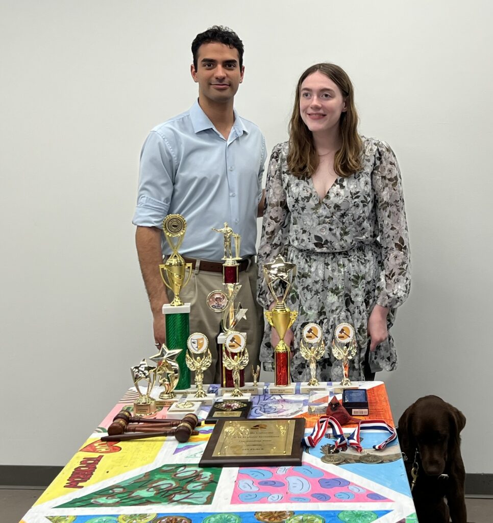 Photo of two team members standing behind a table filled with team trophies.